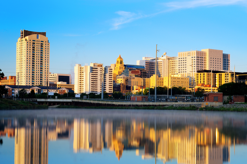 The view of the Rochester skyline from the water. There are lots of buildings at all different heights. You can see the buildings reflecting into the river. 