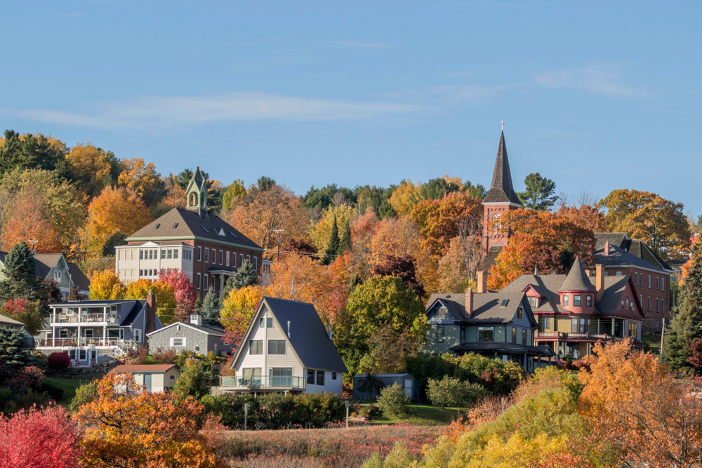 The skyline of one of the cutest small towns in Wisconsin. You can see old homes, buildings, and a church steeple peaking through the tops of trees. The trees have red, yellow, orange, and green leaves on them.