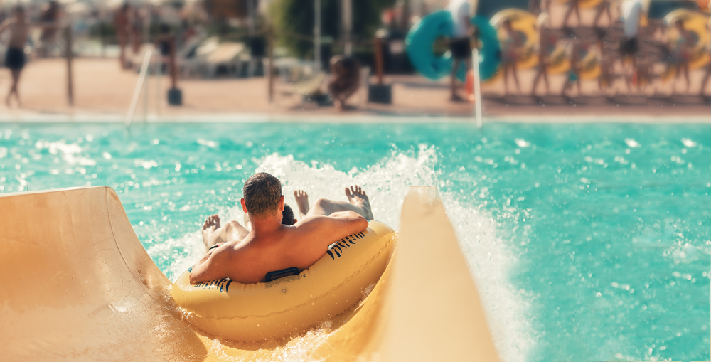 A person in a yellow innertube sliding down the bottom of a waterslide into a pool. The slide is cream and the water in the pool is a pretty aqua blue. One of the best things to do in Wisconsin Dells. 