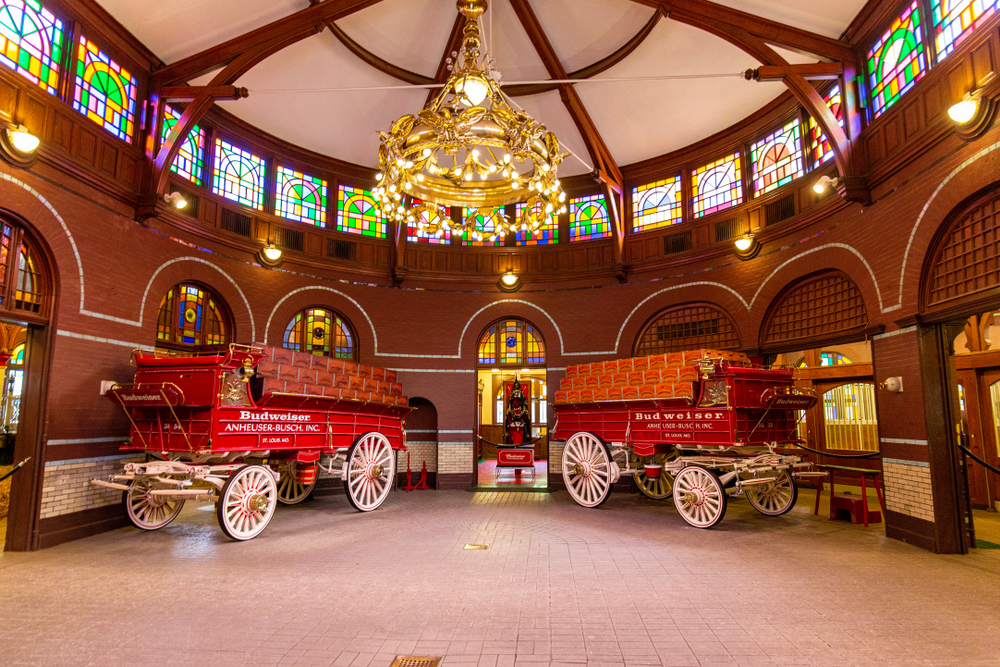 The inside of the Anheuser-Busch Brewery with wagons, a chandelier, and stained glass.