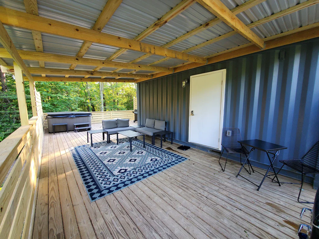 Blue metal container, with wooden porch, blue mosaic rug with table and chairs. Hocking Hills cabins.