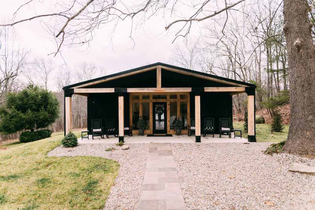 Luxury Cabins in Hocking Hills with black exterior, wood beams and columns, large gravel driveway in forefront.