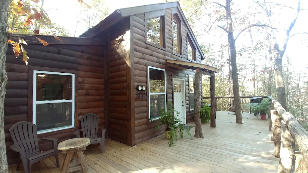 Brown log cabin with large wooden front porch with table and chairs.