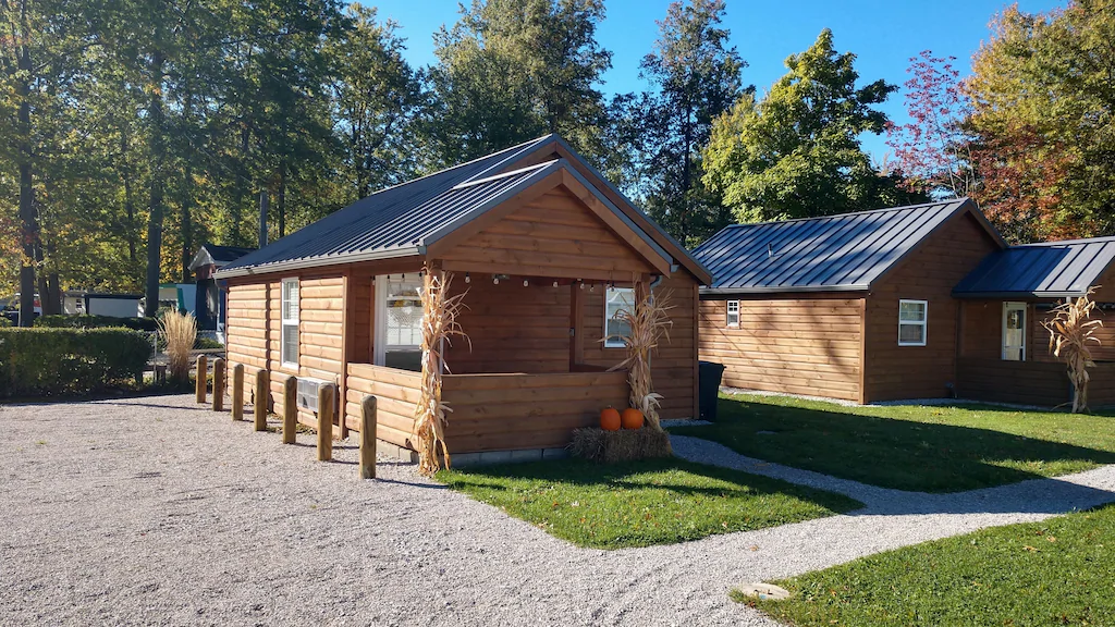 Brown cabin with green roof with front porch. Pumpkin decorations in front. Gravel parking area on left. Ohio cabins.