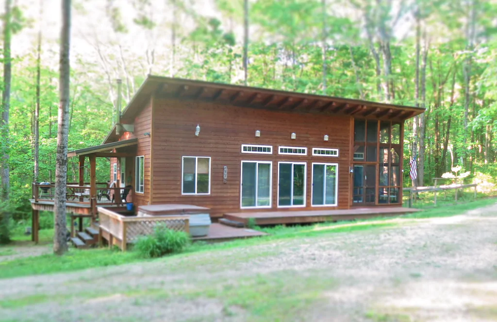 Brown wooden cabin with trees on background. Glass sliding doors, screen porch and balcony. Cabins in Ohio