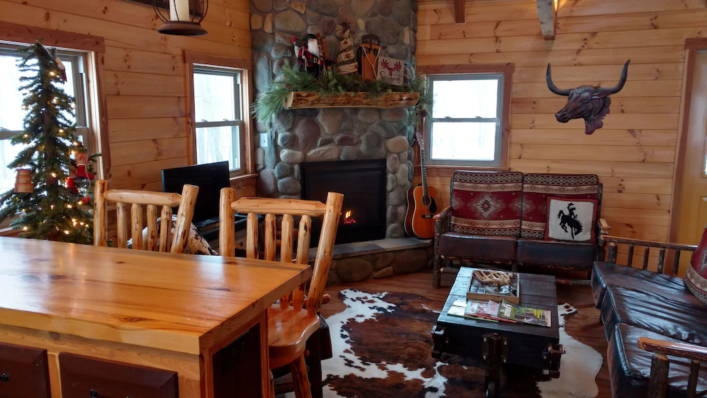 Texas-style cabin living area with log walls, wooden table and chairs, and Christmas tree.