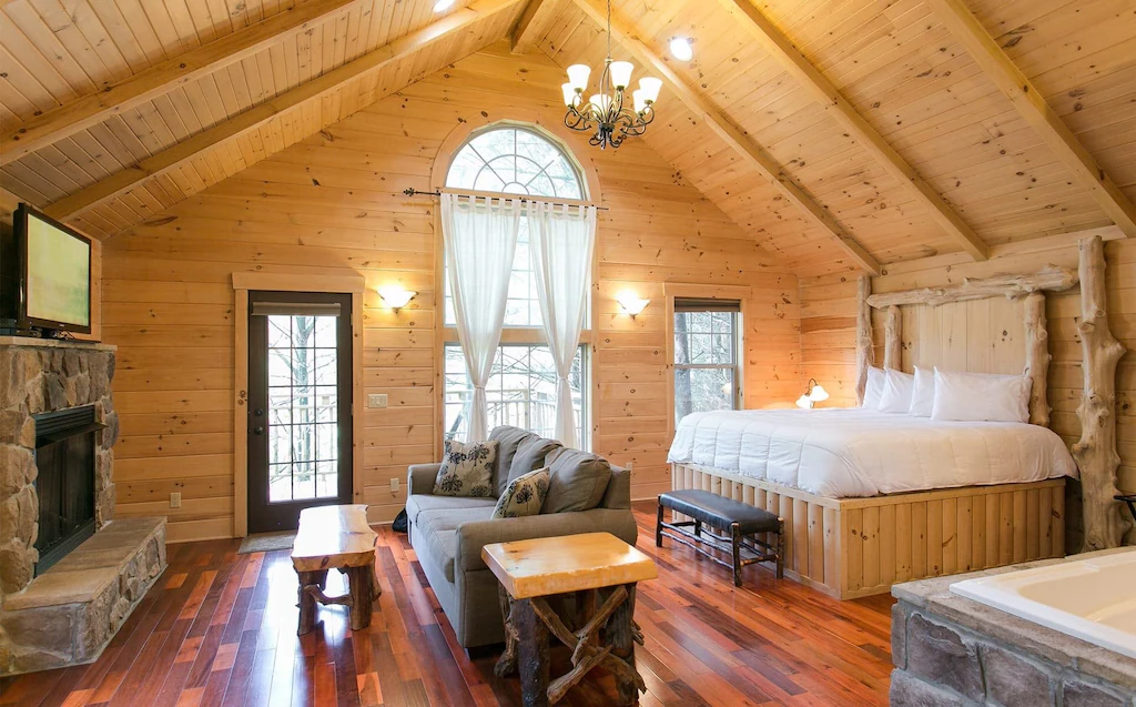 Beautiful room with wooden walls and solid wood floor, grey couch and bed with white bedding.