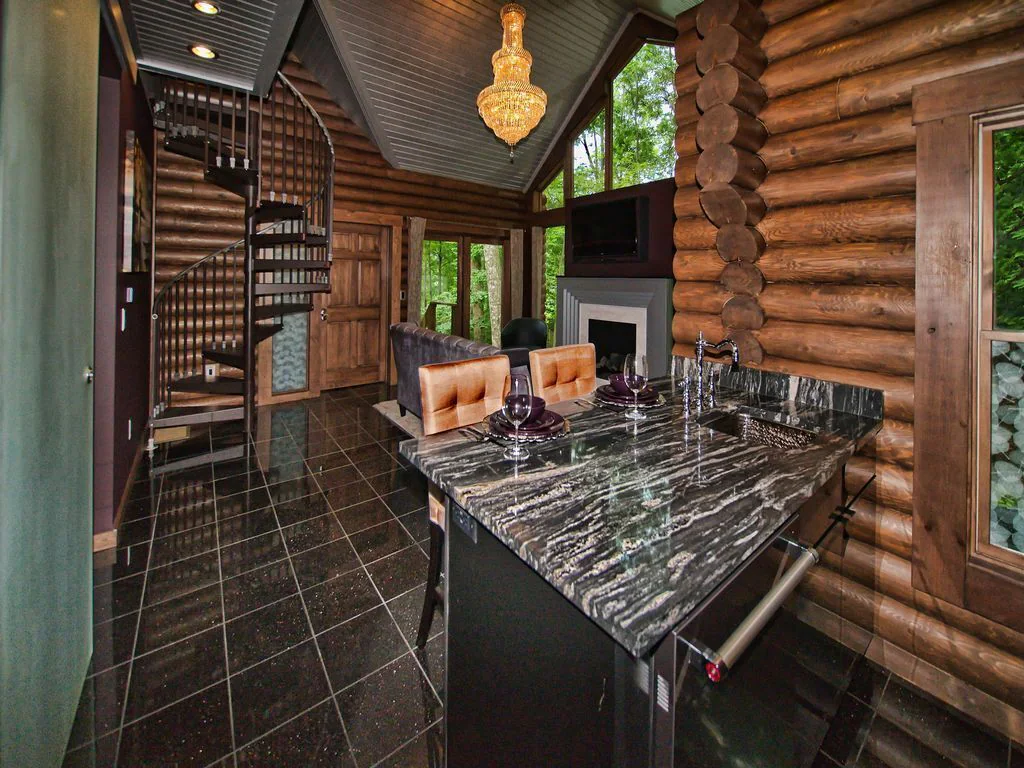 Granite dining table with brown chairs, brown tile floor, log walls and spiral staircase. Cabins in Ohio.