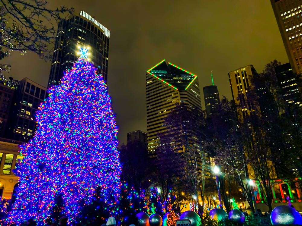 The Christmas tree in Millennium Park with bright, purple lights and skyscrapers in the background at night.