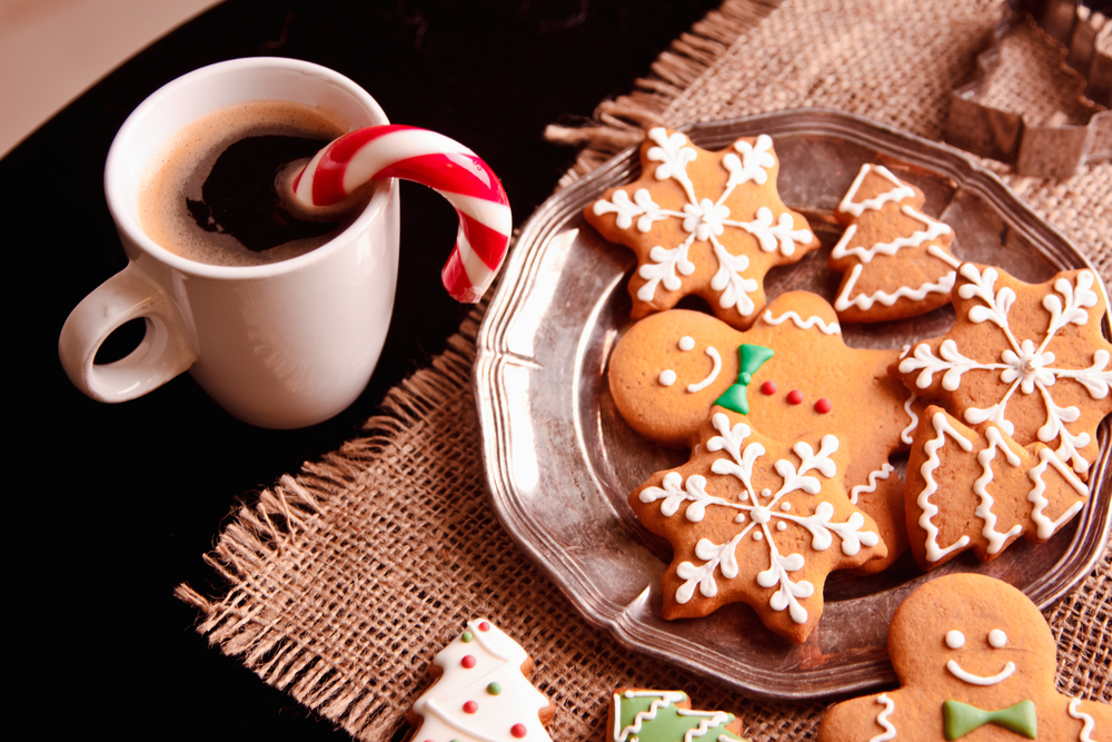 A plate of Christmas cookies on a table next to a mug of hot cocoa with a candy cane.