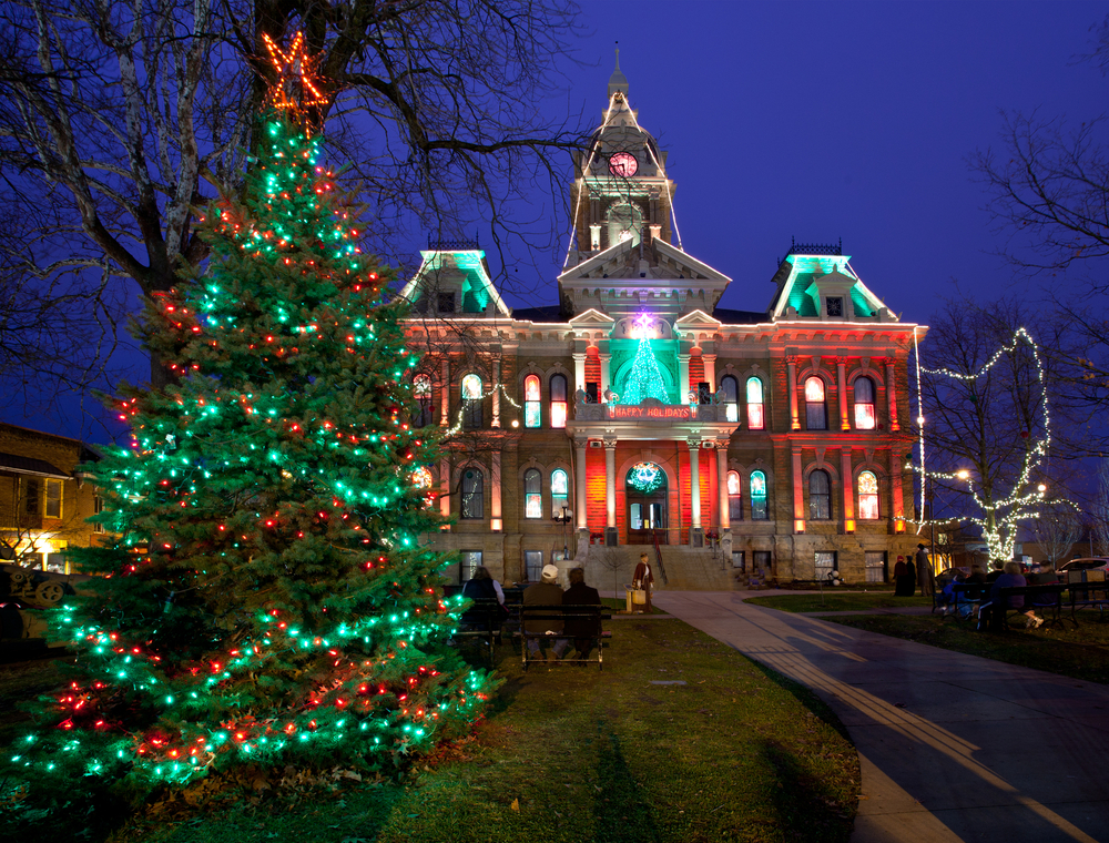 Evergreen tree decorated with red and green lights. Large ornate building in background decorated with red and green lights.