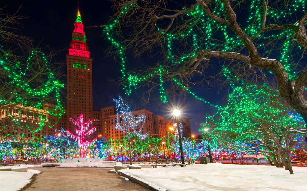 Colorful Ohio Christmas lights on trees with snow on ground. City buildings in background.