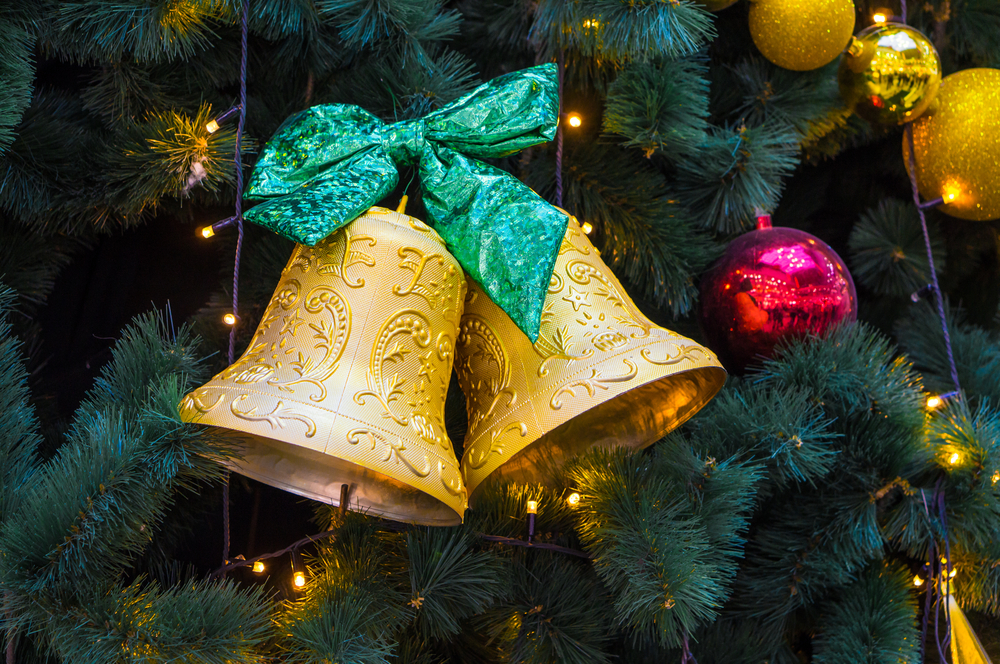 Gold Christmas bells with green ribbon hung on evergreen tree.