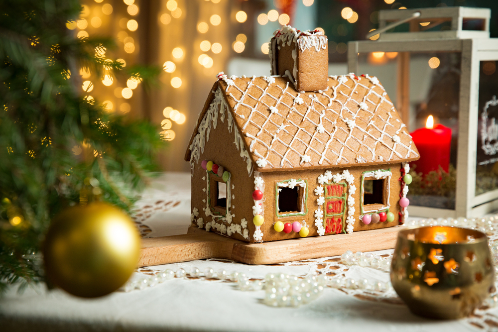 A gingerbread house next to a Christmas tree and candles.