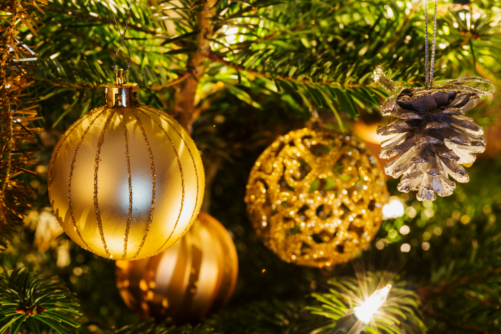 Festive gold ornaments handing from green tree limbs illuminated with white lights.