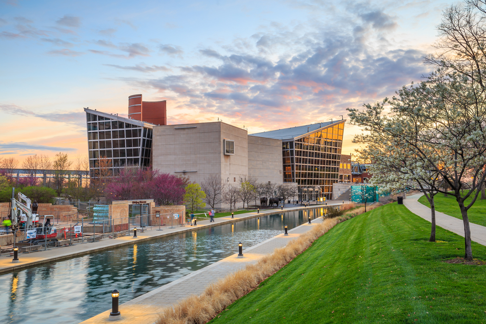 Outside of the Indiana State Museum with a canal in front and flowering trees at sunset.