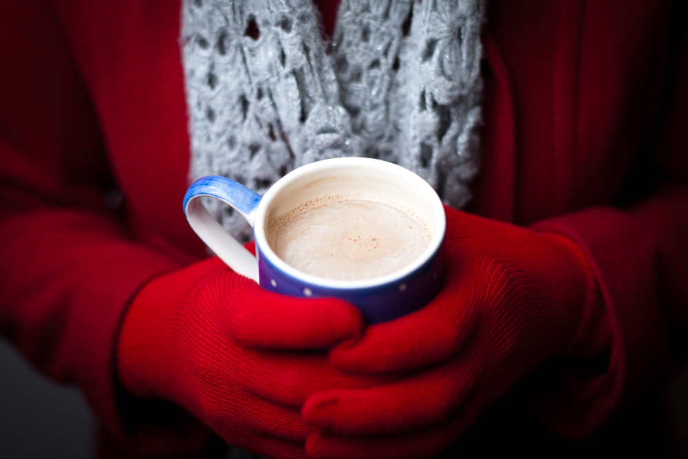 Woman with red gloves holding a mug of hot cocoa.