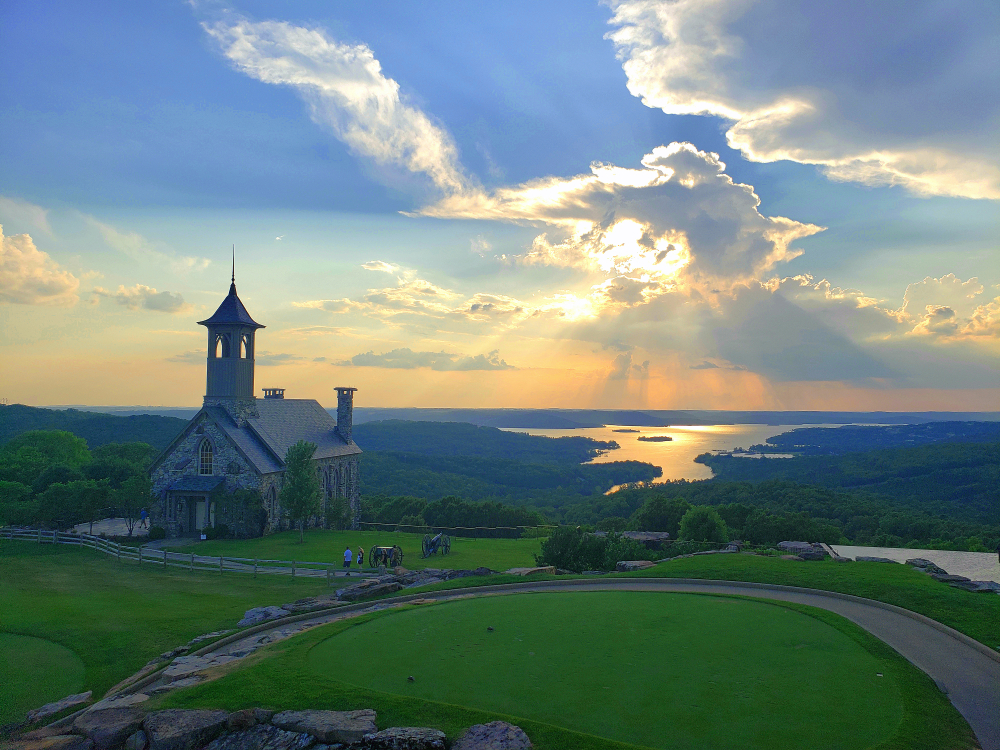 Sunset with orange sky and chapel sitting high on hill with water in distant background.