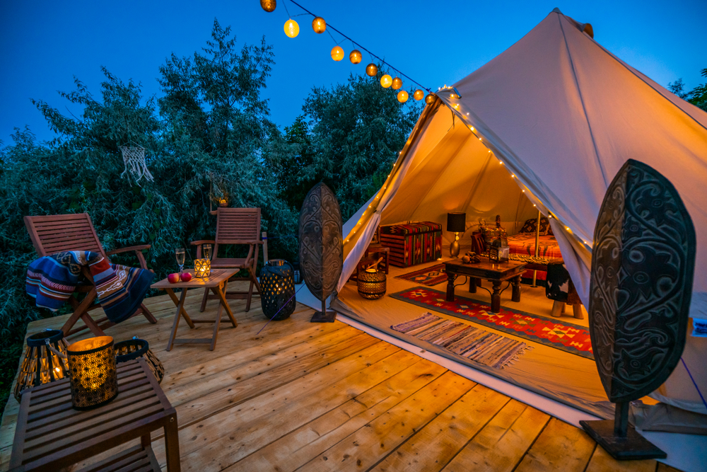 Tent with white romantic white lights and candles on deck with brown patio furniture and glasses of wine with apples.