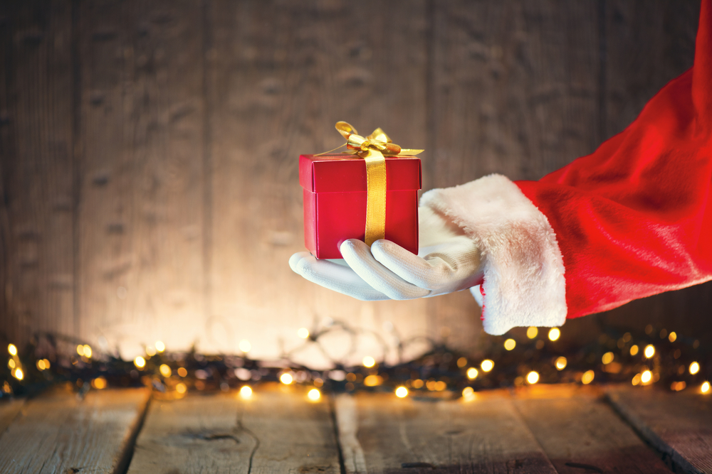 Santa Claus's arm reaching into the frame holding a wrapped present.