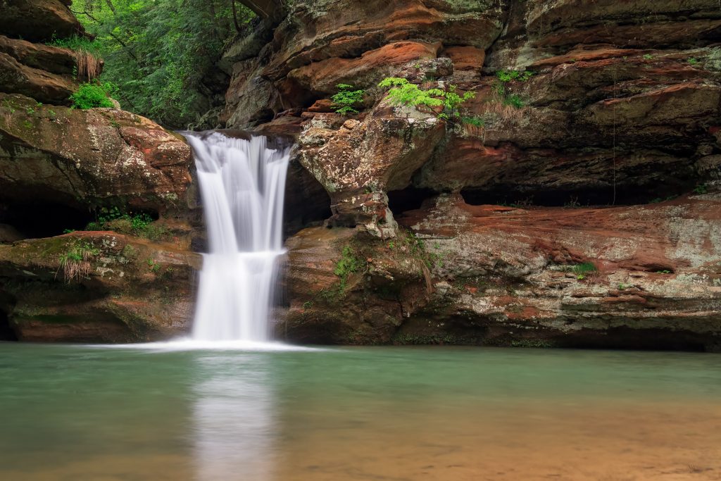 Cascading waterfall pours down over rock formations into pool of still water.