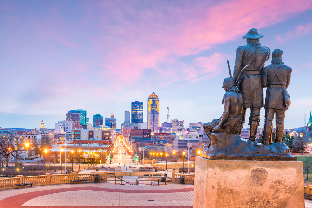 A sculpture of historic figures looking out over the Des Moines skyline at sunset.