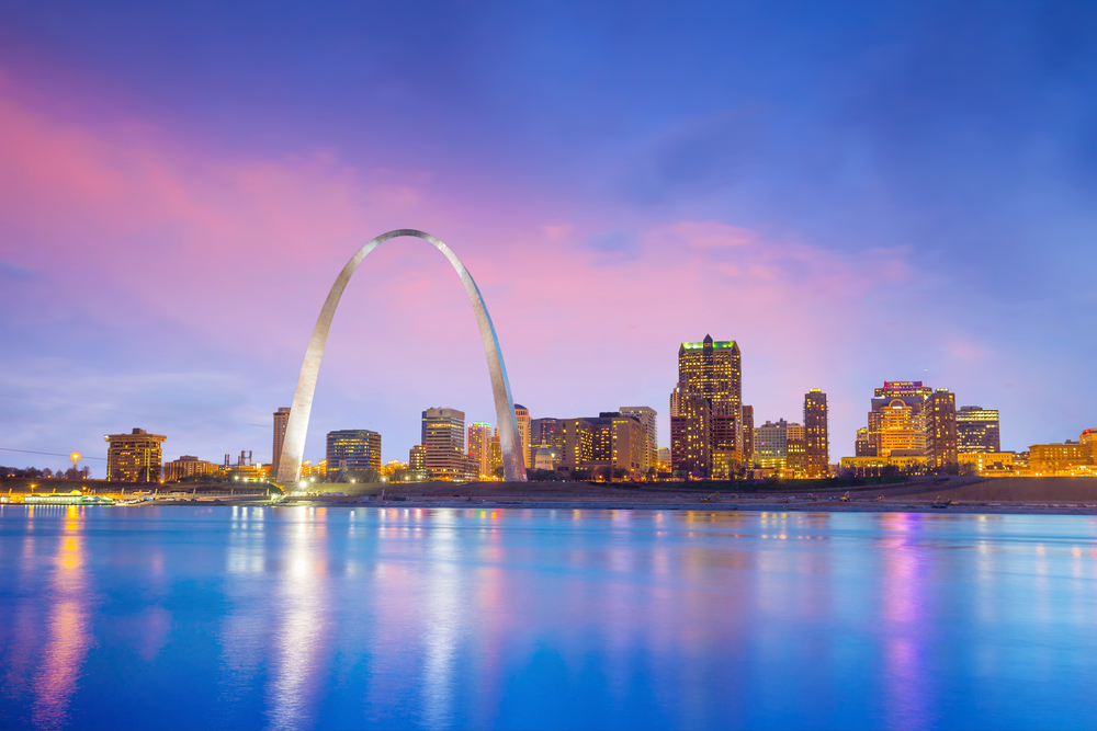 The St. Louis skyline with the Gateway Arch and a pink and purple sky and water.