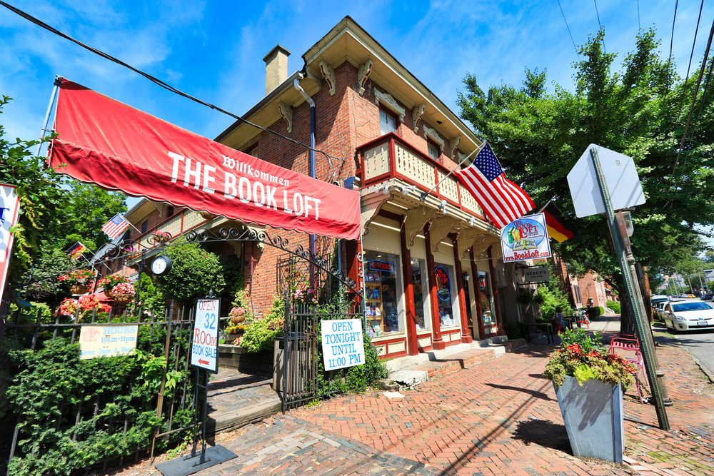 The book loft is pictured on a brick sidewalk.  The store has German balconies and a big red sign that says “Wilkommen The Book Loft”