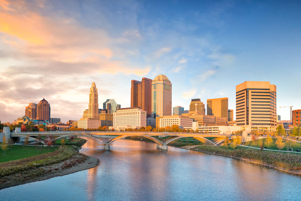 Urban city with tall buildings, bridge over river in forefront.