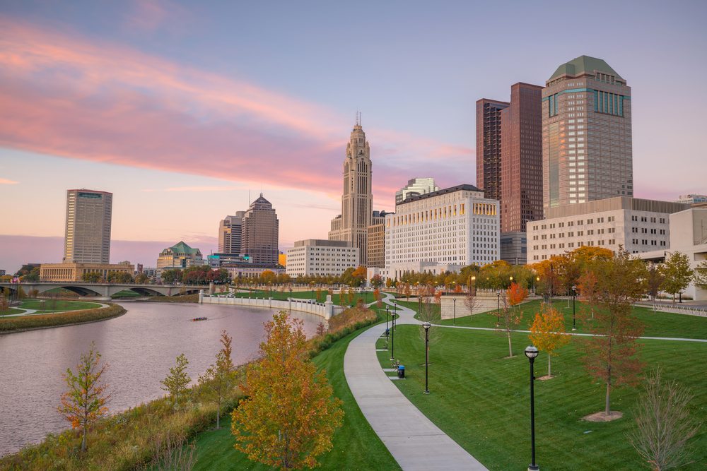 This picture features the urban trails, one of the best things to do in Columbus Ohio.  The trails wind through green spaces and skyscrapers as depicted at sunset in this image.  