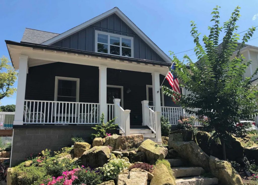Gray house with white trim, white railing and white steps leading up to porch. American flag waving on pillar. Ohio VRBO.