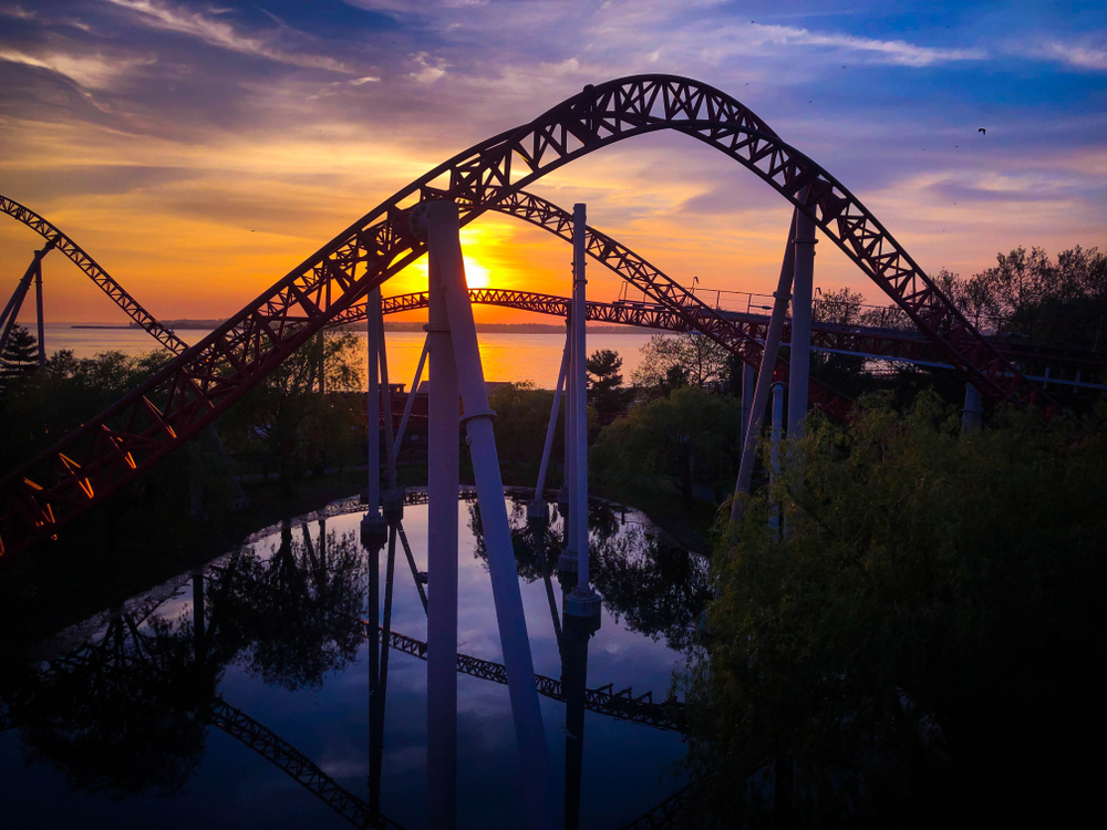 Bright yellow and orange sky over water with roller coaster tracks in foreground. 
Weekend getaways in Ohio