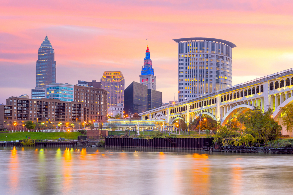 City skyscrapers and arched bridge illuminated with pink sunset sky in background.