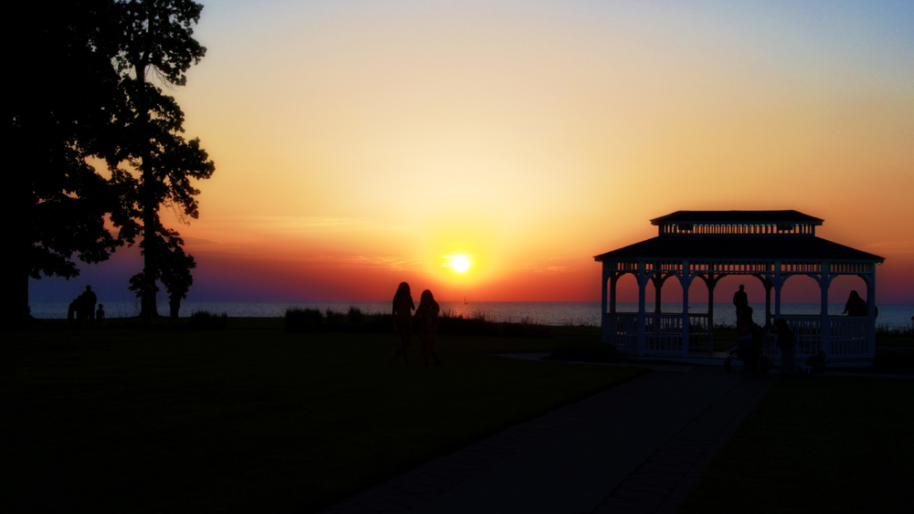 Brilliant orange and yellow sunset with pavilion on right and people on beach in background.