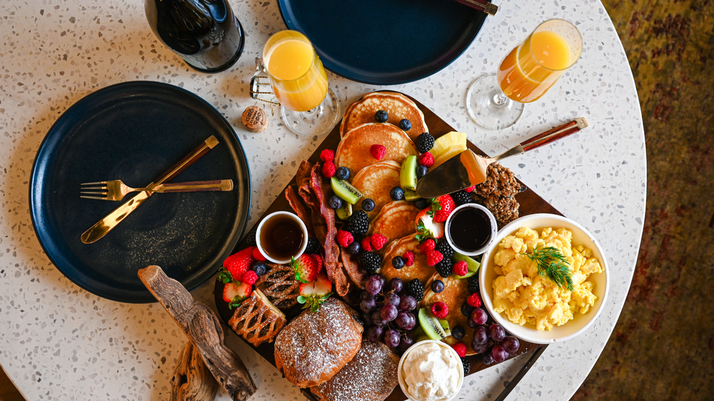 A Brunch platter with pancakes, bacon, eggs and pastries with mimosas