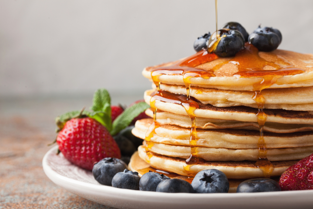 A stack of pancakes with syrup been dribbles on and fruit around the side in an article about breakfast in St Louis