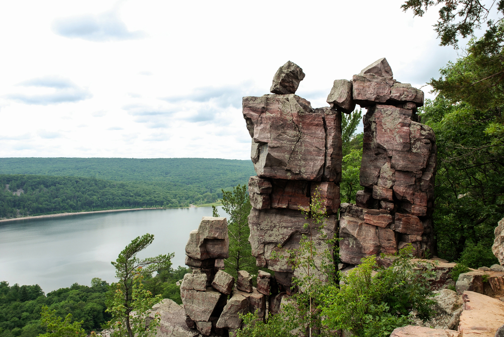 A unique rock formation that looks over Devil's Lake. Behind the rock formation you can see the lake surrounded by hills covered in trees. 