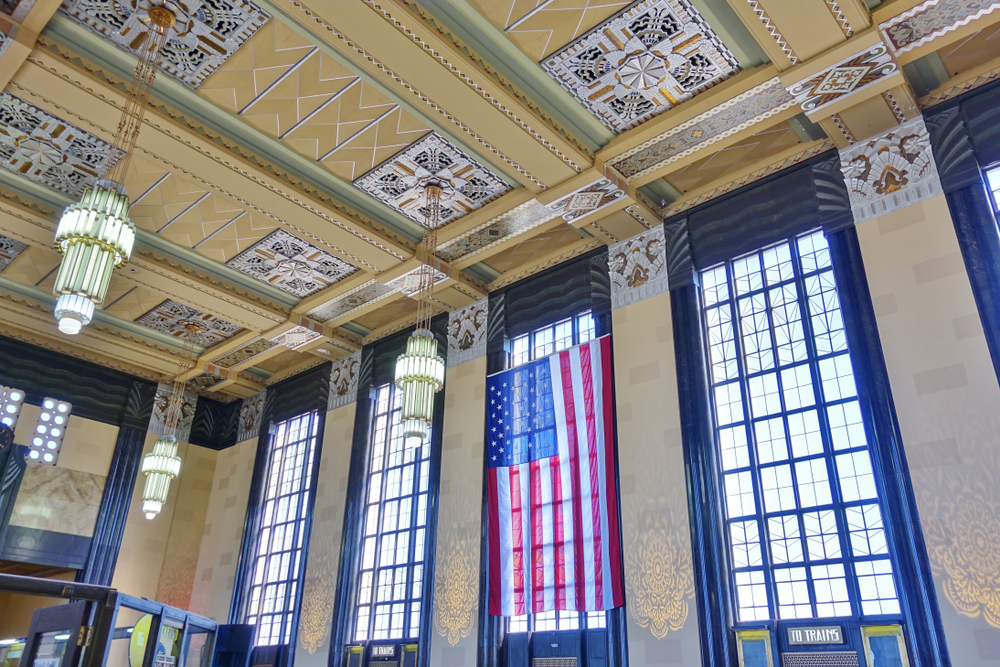 Looking up at the ceiling of an Art Deco building that was once a train station in Omaha. It has large windows on the side of the building, crystal chandeliers, and decorative tiles. 