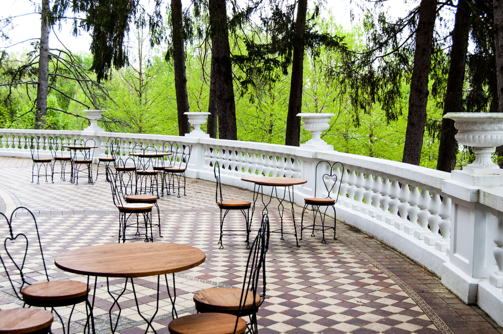 The patio of a historic home in French Lick, one of the best weekend getaways in Indiana. There are metal and wood bistro tables set up, and the patio is parquetted with a white railing with white planters on it. You can see trees past the patio. 