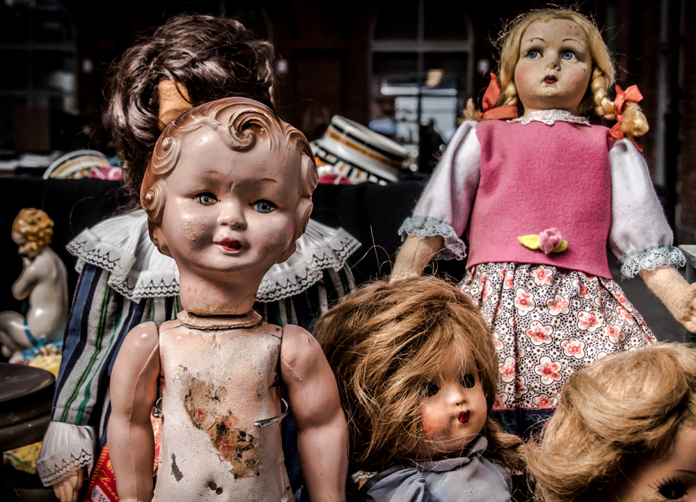 A collection of creepy dolls. They are plastic and porcelain. Some of them have hair and clothes and some do not. 