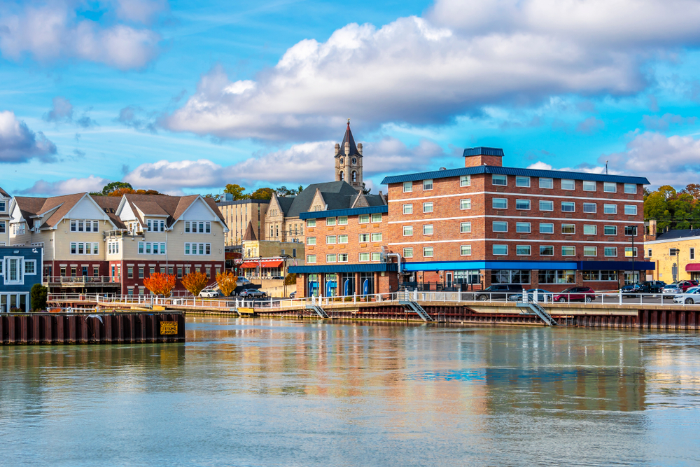 Looking at a port town that has some brick buildings, a church steeple, and a marina. The sky is very blue with big fluffy clouds. Its a great stop on Wisconsin road trips. 