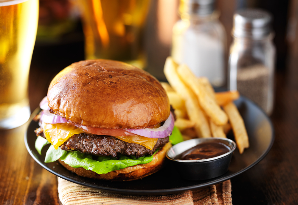 Cheeseburger on a plate with fries and a side of sauce.