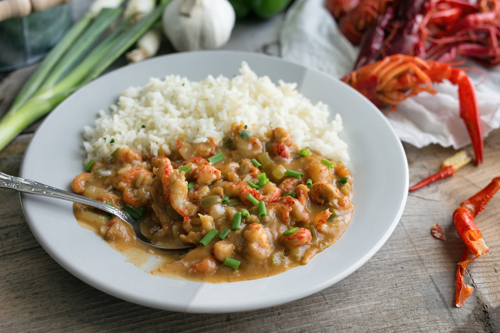 Crawfish Étouffée on a plate with rice and some crawfish shells and spring onions in the background