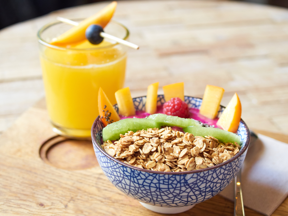 A acacia bowl on a table with a glass of orange juice