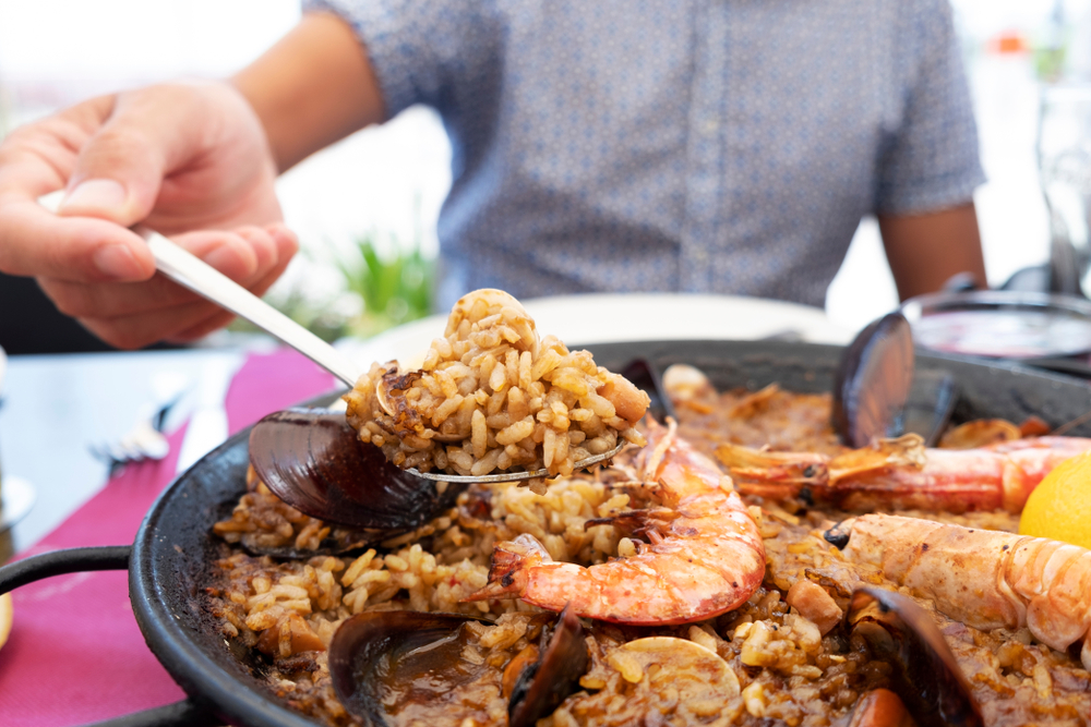 close up of a person with a spoonful o paella coming from the paella dish.