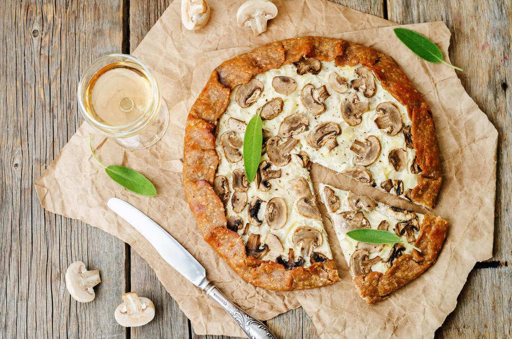 A mushrooms pizza on a table with cut mushrooms a knife and a glass of wine