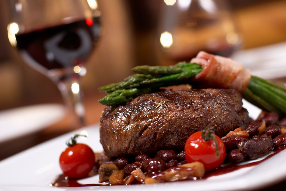 A steak on aplate with tomatoes and asparagus and a sauce