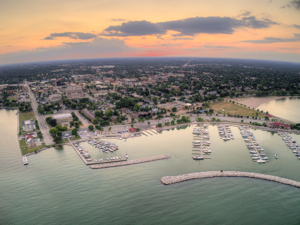 An aerial view of Sturgeon Bay, the biggest city in Door County. You can see a large marina with boats, a beach and grassy area on the lake, and lots of buildings surrounded by trees. A great place for Wisconsin road trips.