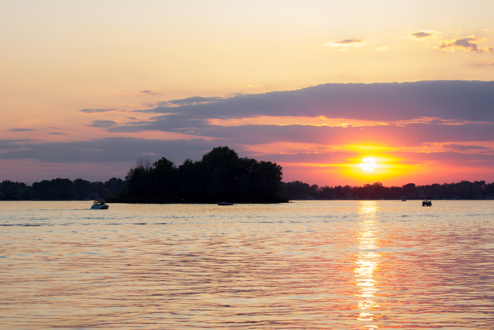 Brilliant yellow sunset with trees in background and calm waters in foreground.