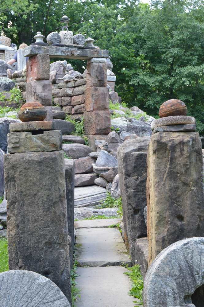 The entrance of a man made temple that's one of the most unique hidden gems in Ohio. It is made out of different sizes and types of rocks. Behind the temple you can a dense forest and there is grass growing in the cracks of rocks. 